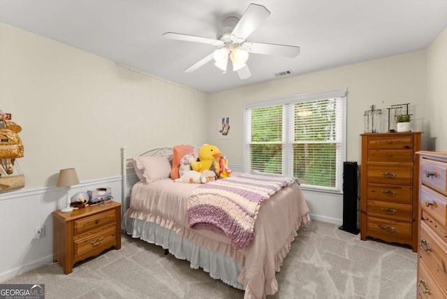 bedroom with light colored carpet, a wainscoted wall, and a ceiling fan