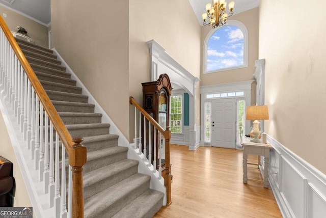 entrance foyer featuring a high ceiling, stairway, light wood-type flooring, a chandelier, and wainscoting