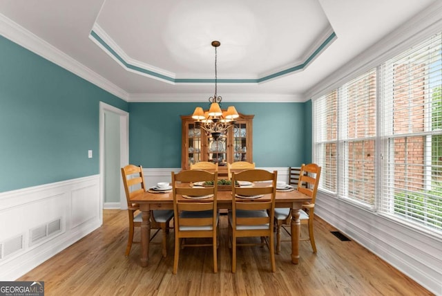 dining space featuring a tray ceiling, a chandelier, wood finished floors, a wainscoted wall, and ornamental molding