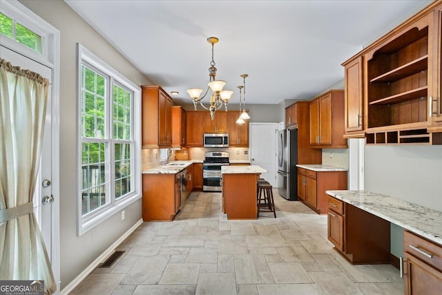 kitchen with stainless steel appliances, a chandelier, stone tile floors, brown cabinets, and a breakfast bar