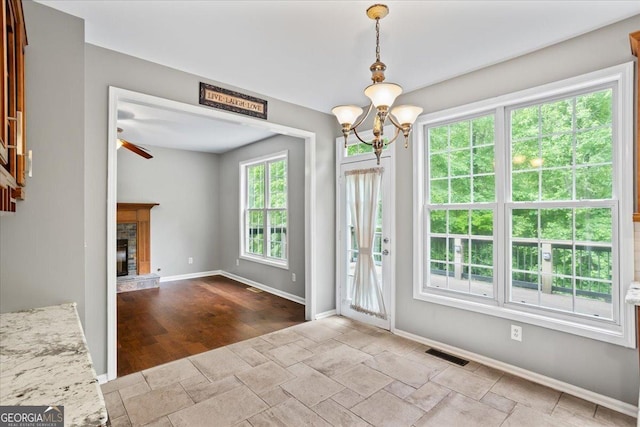 unfurnished dining area featuring ceiling fan, a chandelier, a stone fireplace, baseboards, and stone finish flooring