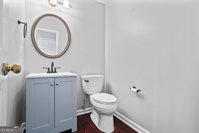 half bathroom featuring baseboards, toilet, vanity, and wood finished floors