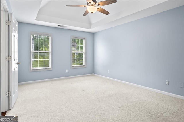 carpeted spare room with a raised ceiling, a ceiling fan, and baseboards