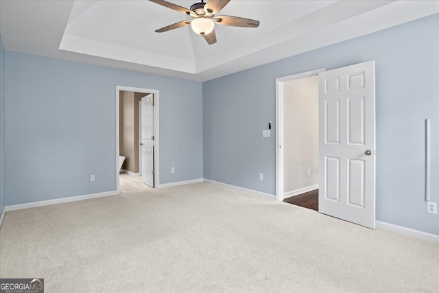 unfurnished bedroom featuring carpet floors, a tray ceiling, baseboards, and ceiling fan
