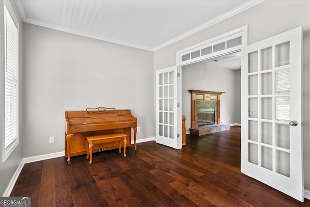 living area featuring crown molding, hardwood / wood-style floors, baseboards, french doors, and a stone fireplace