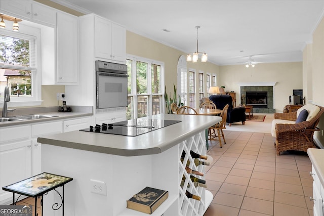 kitchen with oven, a sink, black electric stovetop, a tiled fireplace, and open floor plan