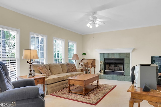 living room featuring ceiling fan, ornamental molding, a tile fireplace, and carpet flooring