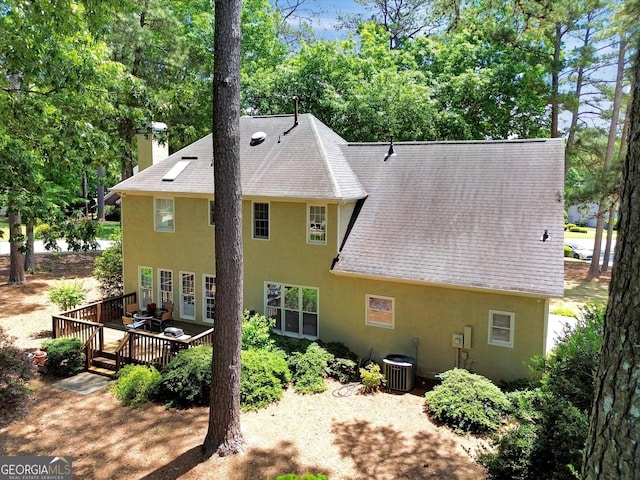 back of property featuring stucco siding, a shingled roof, a deck, central air condition unit, and a chimney