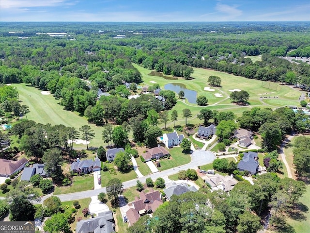 aerial view of property and surrounding area with a golf course, a nearby body of water, a forest, and nearby suburban area
