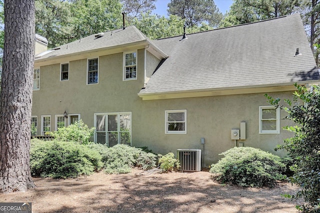 rear view of property featuring stucco siding, cooling unit, and roof with shingles