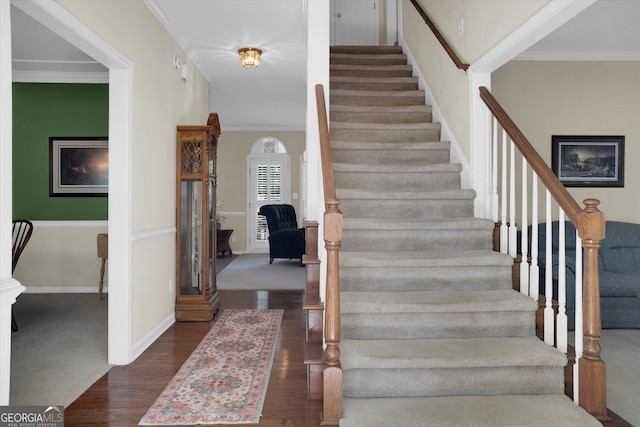 staircase with wood finished floors, crown molding, and baseboards