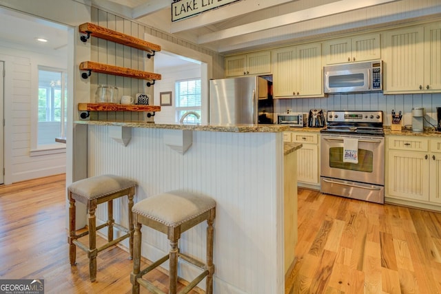 22 Waters Bridge Cir, Covington, GA 30014 - kitchen featuring appliances with stainless steel finishes, a breakfast bar area, light wood-type flooring, light stone counters, and beamed ceiling