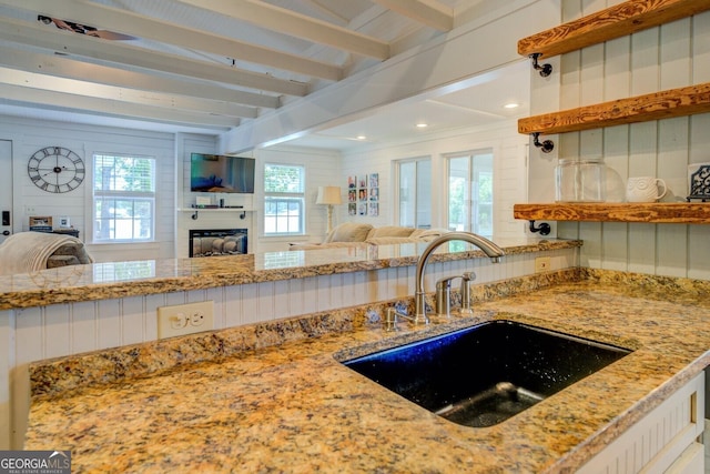 22 Waters Bridge Cir, Covington, GA 30014 - kitchen featuring open floor plan, a glass covered fireplace, a sink, beam ceiling, and light stone counters