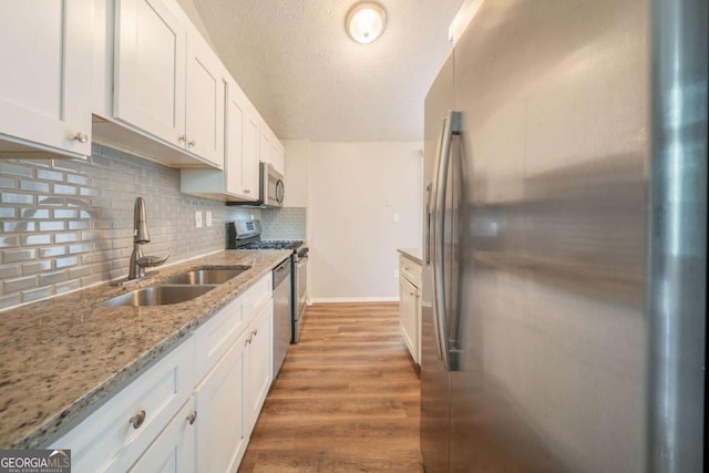 kitchen with appliances with stainless steel finishes, a sink, white cabinets, light wood-style flooring, and backsplash
