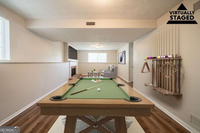 playroom featuring wood finished floors, baseboards, a textured ceiling, a fireplace with raised hearth, and pool table