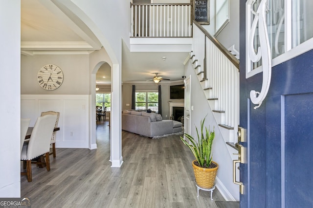 foyer with arched walkways, a ceiling fan, wood finished floors, a towering ceiling, and a fireplace