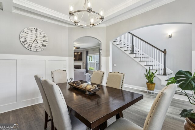 dining space featuring arched walkways, a raised ceiling, a chandelier, stairs, and wood finished floors