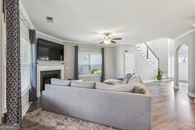 living area featuring arched walkways, a ceiling fan, wood finished floors, a tiled fireplace, and ornamental molding