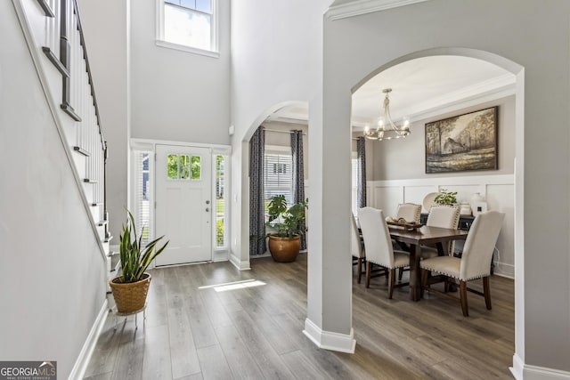 entryway featuring wood finished floors, crown molding, arched walkways, a towering ceiling, and a chandelier