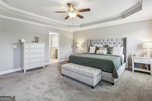 carpeted bedroom featuring a raised ceiling, ornamental molding, baseboards, a ceiling fan, and ensuite bathroom