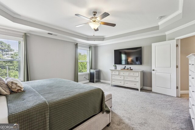 carpeted bedroom featuring a tray ceiling, ornamental molding, ceiling fan, and baseboards