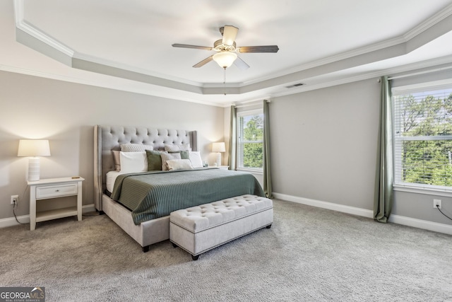 carpeted bedroom with a tray ceiling, crown molding, multiple windows, baseboards, and a ceiling fan