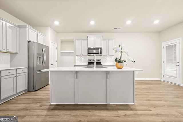 116 Cabin Way, Hampton, GA 30228 - kitchen featuring appliances with stainless steel finishes, light countertops, decorative backsplash, a center island with sink, and light wood-style flooring