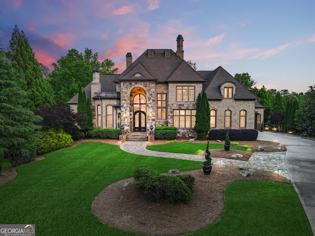 french country home featuring a front lawn, french doors, a chimney, stone siding, and curved driveway