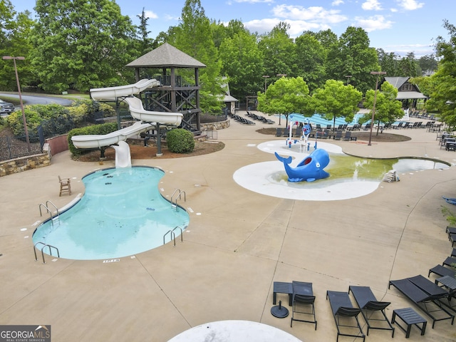 community pool featuring a water slide, view of wooded area, and a patio