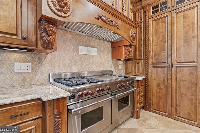 kitchen featuring double oven range, brown cabinets, backsplash, light stone countertops, and glass insert cabinets