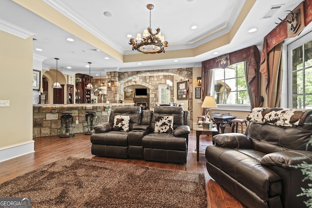 living room with a raised ceiling, crown molding, a chandelier, wood finished floors, and a fireplace