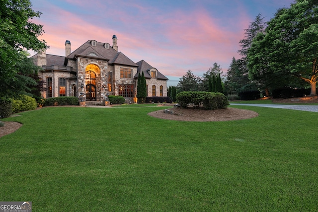 french country home featuring stone siding, a lawn, and a chimney