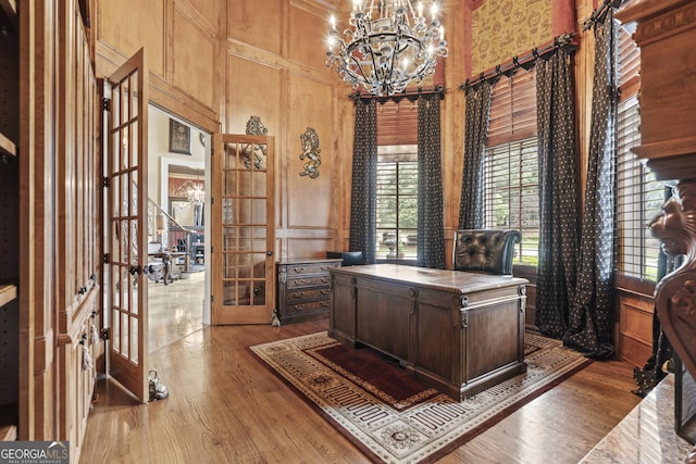 office space featuring french doors, a chandelier, wood finished floors, a high ceiling, and a decorative wall