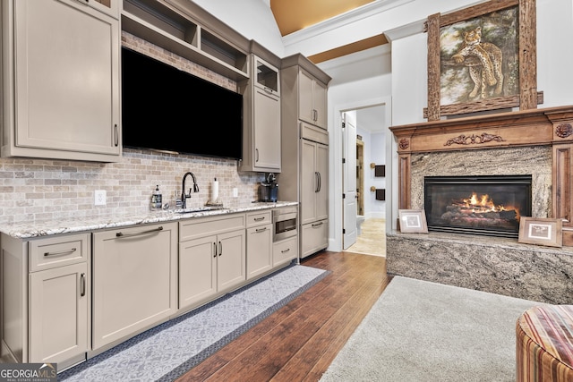 kitchen featuring a sink, dark wood-type flooring, paneled built in fridge, decorative backsplash, and a premium fireplace