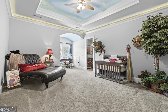 carpeted bedroom featuring a tray ceiling, arched walkways, and a ceiling fan