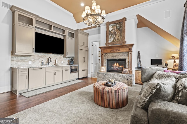 living room with a high end fireplace, dark wood-style floors, a chandelier, and vaulted ceiling