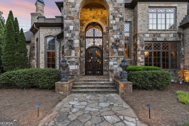 entrance to property featuring french doors, stone siding, and brick siding