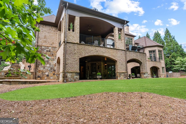 rear view of property featuring a balcony, brick siding, a lawn, and stone siding