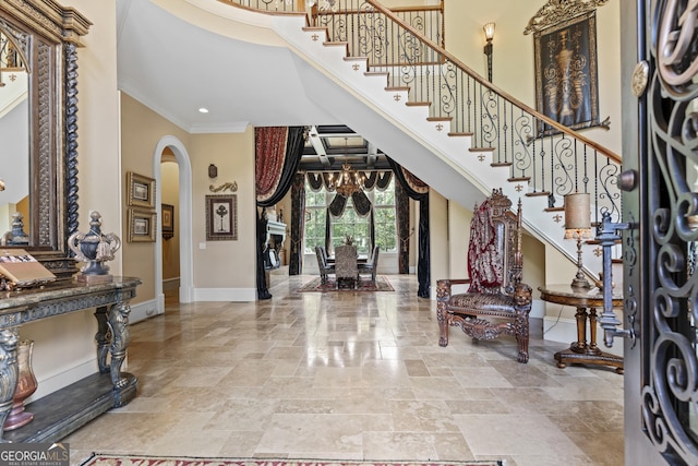 foyer with arched walkways, ornamental molding, baseboards, a towering ceiling, and stone tile flooring