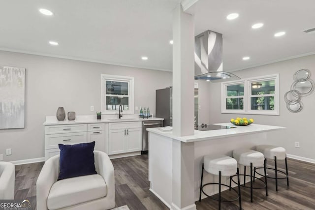 kitchen featuring a sink, dishwasher, a kitchen bar, wall chimney range hood, and white cabinetry