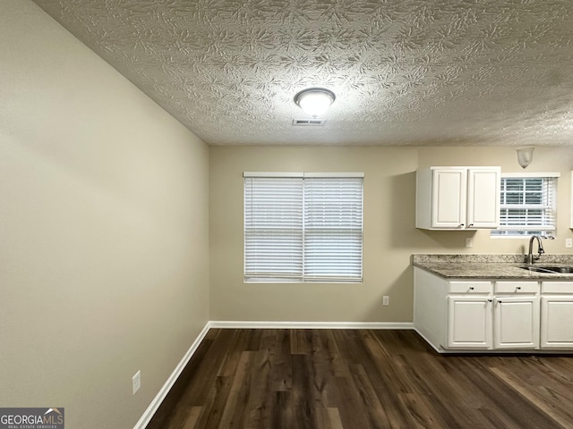9151 Jefferson Village Dr SW, Covington, GA 30014 - kitchen with dark wood-style flooring, white cabinetry, a sink, baseboards, and healthy amount of natural light
