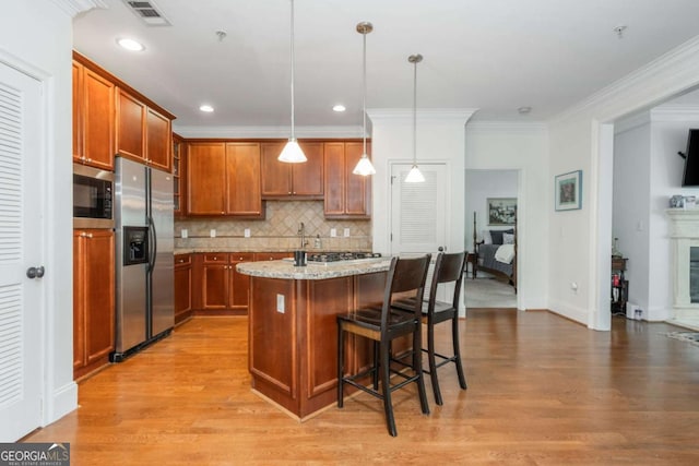 kitchen with appliances with stainless steel finishes, light wood finished floors, light stone countertops, brown cabinets, and crown molding
