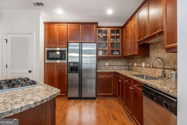 kitchen featuring stainless steel appliances, a sink, ornamental molding, light stone counters, and light wood-style floors