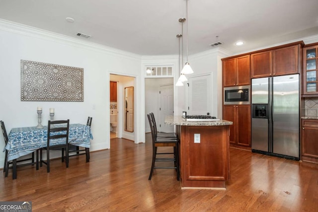 kitchen with appliances with stainless steel finishes, ornamental molding, a kitchen breakfast bar, dark wood-style floors, and a center island