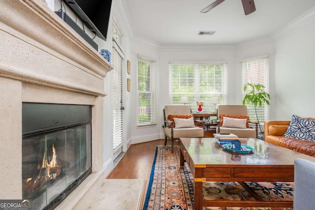 living room with a fireplace, wood finished floors, crown molding, ceiling fan, and baseboards