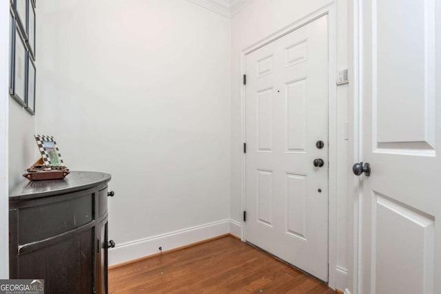 doorway featuring wood finished floors, ornamental molding, and baseboards