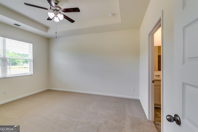 spare room featuring a raised ceiling, ceiling fan, light carpet, and baseboards