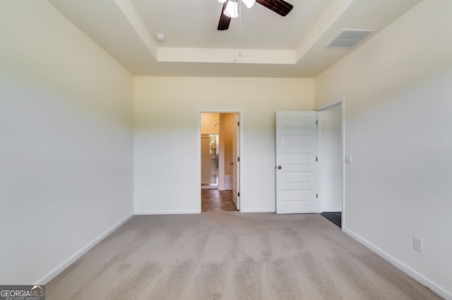 unfurnished bedroom featuring a raised ceiling, carpet flooring, baseboards, ensuite bath, and ceiling fan