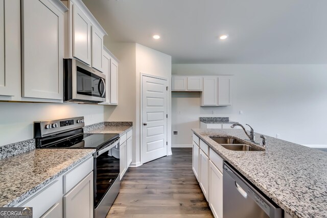 kitchen featuring stainless steel appliances, a sink, dark wood finished floors, light stone countertops, and white cabinets