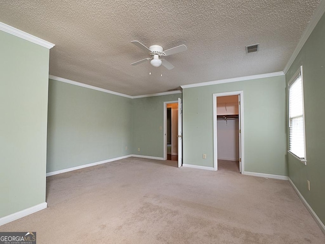 unfurnished bedroom featuring carpet flooring, crown molding, baseboards, a walk in closet, and a textured ceiling